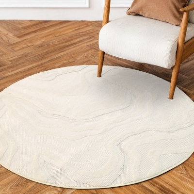 Tapete redondo branco com padrão texturizado colocado sob cadeira de madeira com assento e almofada bege.
