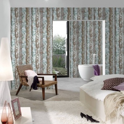 Quarto moderno com papel de parede madeira azul e branco, poltrona de vime castanha, cama com cobertores bege e roxo e luminária branca.