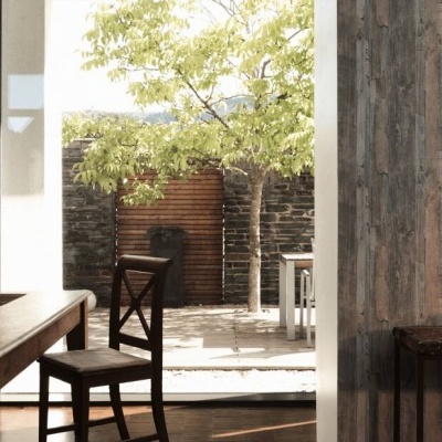 Sala rústica com mesa e cadeira junto à porta aberta para pátio ensolarado