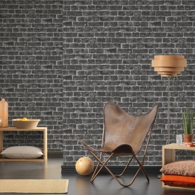 Cadeira marrom com estrutura metálica, lâmpada suspensa de madeira, suportes de madeira com almofadas e planta, parede de tijolos cinzentos