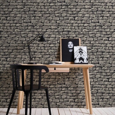Escritório com mesa de madeira clara, cadeira preta e parede com padrão de pedras cinzentas