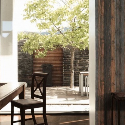 Sala de jantar com mesa e cadeira de madeira, papel parede riscado e porta aberta para pátio com árvore.