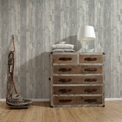 Cómoda rústica com cinco gavetas e lâmpada de mesa branca sobre ela, parede cinzenta texturizada tipo madeira e chão de madeira clara