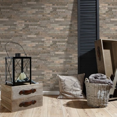 Espaço decorado com parede de tijolos artificiais castanhos, almofada, cesto com manta, caixa de madeira e lanterna preta.