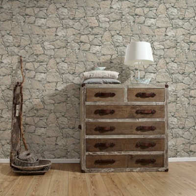 Cómoda de madeira envelhecida com gavetas e ferragens, almofadas e lâmpada branca, parede com papel de parede de pedras cinzentas