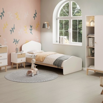 Quarto infantil com mobília branca e madeira clara, roupa de cama bege e cinza, parede rosa decorada, e brinquedos no chão