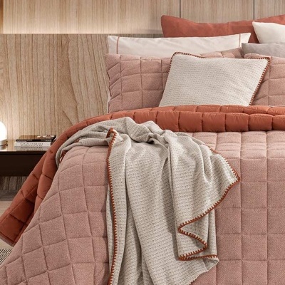 Cama com roupa de cama em tons terracota e bege, e manta bege com borda terracota