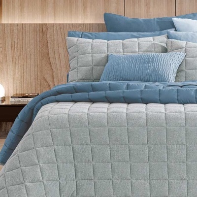 Cama com edredão e almofadas azuis e cinzentas com padrão quadrado e cabeceira de madeira