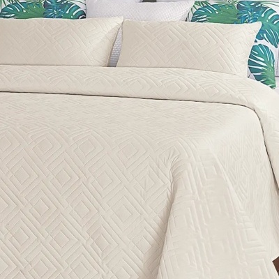Cama com colcha bege com padrão geométrico e almofadas estampadas com folhas verdes e azuis