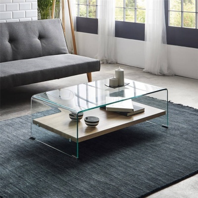 Mesa de centro em vidro e madeira numa sala com sofá cinzento e janelas grandes