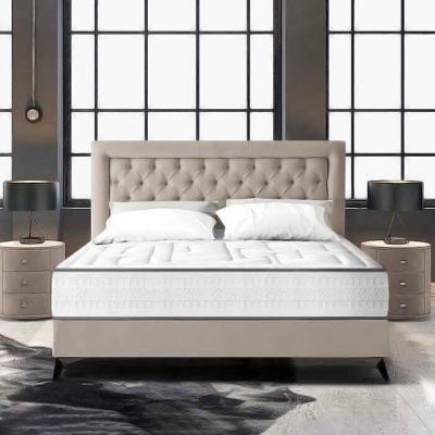 Cama de casal com cabeceira estofada bege e colchão branco em quarto moderno.