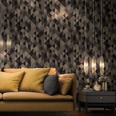 Sala de estar com sofá mostarda, almofadas amarelas e cinzas, mesa preta e luminárias pendentes junto a uma parede geométrica cinza.