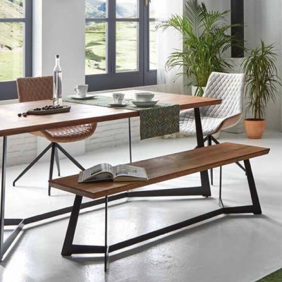 Mesa de madeira com bancos metálicos e cadeiras acolchoadas numa sala iluminada por janela grande