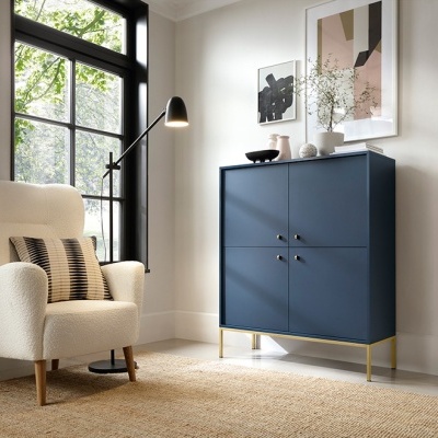 Cadeira branca estofada, cómoda azul escura com pés dourados, tapete natural, lâmpada de chão preta e quadro moderno em sala clara