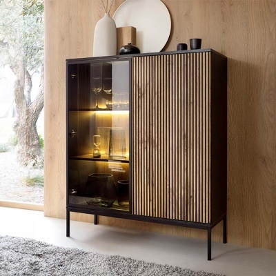 Móvel em madeira escura com porta de ripas verticais e vidro fumado iluminado numa sala com parede de madeira clara.