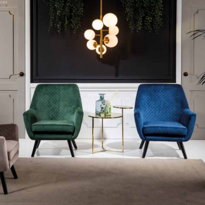 Duas cadeiras estofadas verde e azul com mesa lateral dourada e candeeiro suspenso numa sala elegante