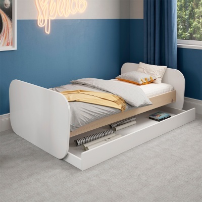 Cama individual branca com gaveta inferior aberta e roupa de cama cinzenta e bege numa divisão com paredes azuis e cortina azul.