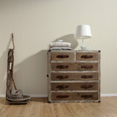 Cómoda vintage em madeira com cinco gavetas e puxadores escuros, candeeiro branco e almofadas com chão de madeira e parede bege.