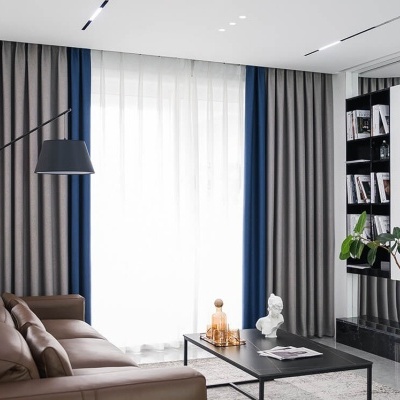 Sala de estar com sofá de couro castanho, cortinas azul e cinza, mesa de centro preta com decoração e estante com livros