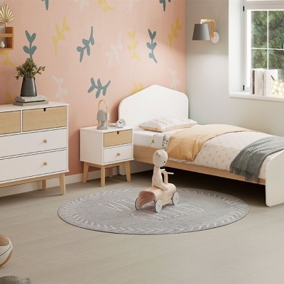 Quarto infantil com cama, cómoda e mesa de cabeceira em madeira clara e branco, decoração de parede floral abstrata e tapete redondo cinzento