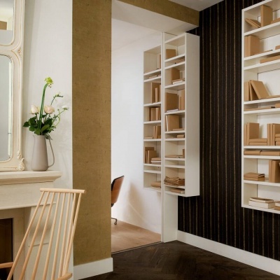 Sala decorada com prateleiras brancas, cadeira de madeira, lareira branca, espelho e vaso com flores