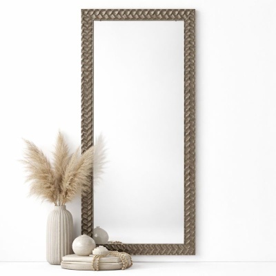 Espelho retangular com moldura castanha texturizada, vaso com penas e objetos decorativos no chão.