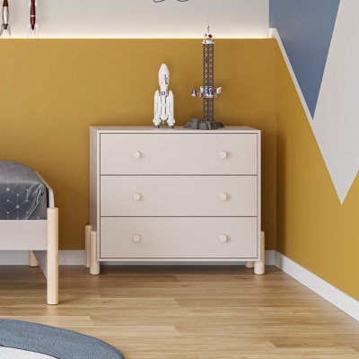 Cómoda branca de três gavetas em quarto com parede mostarda e cinza, chão de madeira clara, com brinquedos em cima