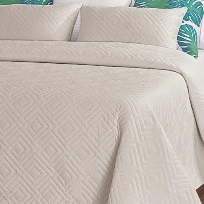 Colcha bege com padrão geométrico e almofadas com padrões variados numa cama