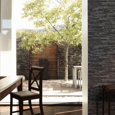 Sala com mobiliário em madeira e parede de pedra escura com vista para a árvore exterior