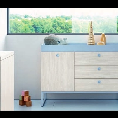 Móvel infantil em madeira clara e azul com gavetas e porta, decorado, junto a janela