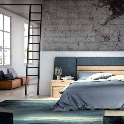 Quarto moderno com cama de casal azul e madeira clara, mesas de cabeceira com candeeiros, cómoda, poltrona e janela grande