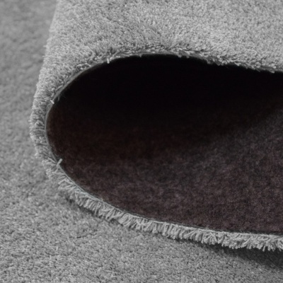 Tapete cinzento claro enrolado mostrando verso mais escuro e franjas