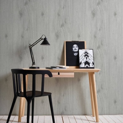 Secretária de madeira clara com cadeira preta, lâmpada de mesa, quadros e parede cinzenta