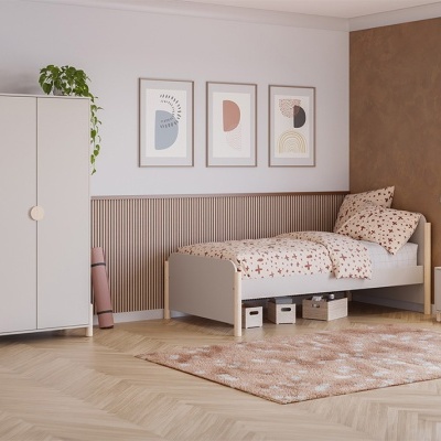 Quarto com cama de solteiro branca, roupa de cama estampada e armário branco com planta