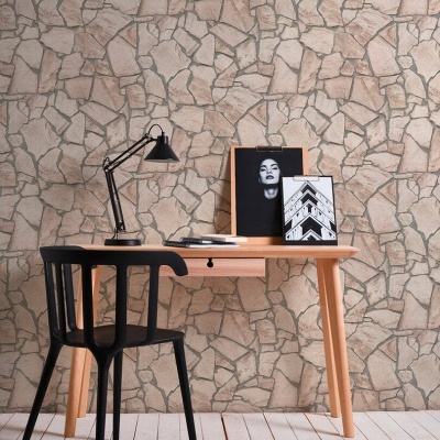 Escrivaninha de madeira clara com cadeira preta, lâmpada de mesa preta e quadros decorativos em parede de pedra bege