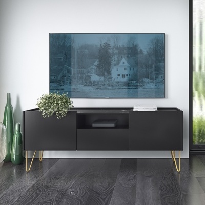 Móvel preto com pernas douradas, TV montada na parede, garrafas verdes e planta decorativa em ambiente moderno