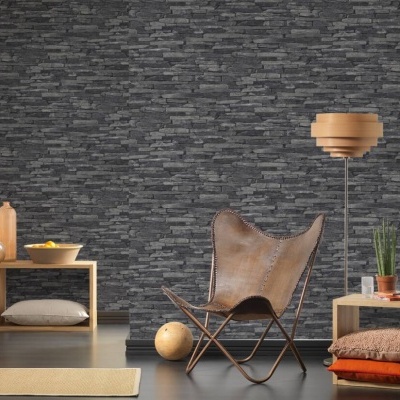 sala com parede de pedra escura, cadeira de couro castanho, candeeiro de madeira, mesa de apoio com plantas e mantas, prateleira com objetos e almofada