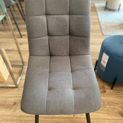 Cadeira cinzenta acolchoada com pernas pretas em ambiente interior com chão de madeira