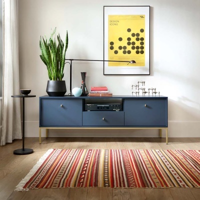 Móvel azul escuro com base dourada, planta em vaso preto, decoração, quadro amarelo DESIGN ICONS e tapete riscado colorido
