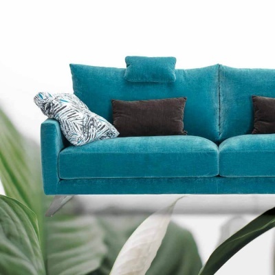 Sofá azul turquesa com almofadas decorativas e pernas metálicas sobre fundo branco e folhas verdes