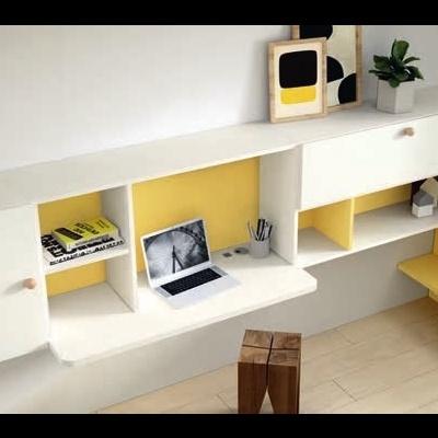 Móvel branco de parede com prateleiras interiores amarelas, portátil aberto, livros e planta, banco amarelo ao lado