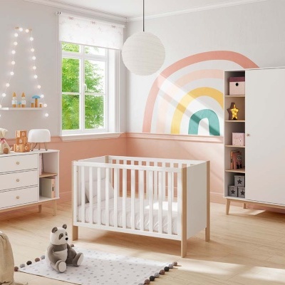 Quarto de bebé com móveis brancos e madeira clara e parede com arco-íris colorido
