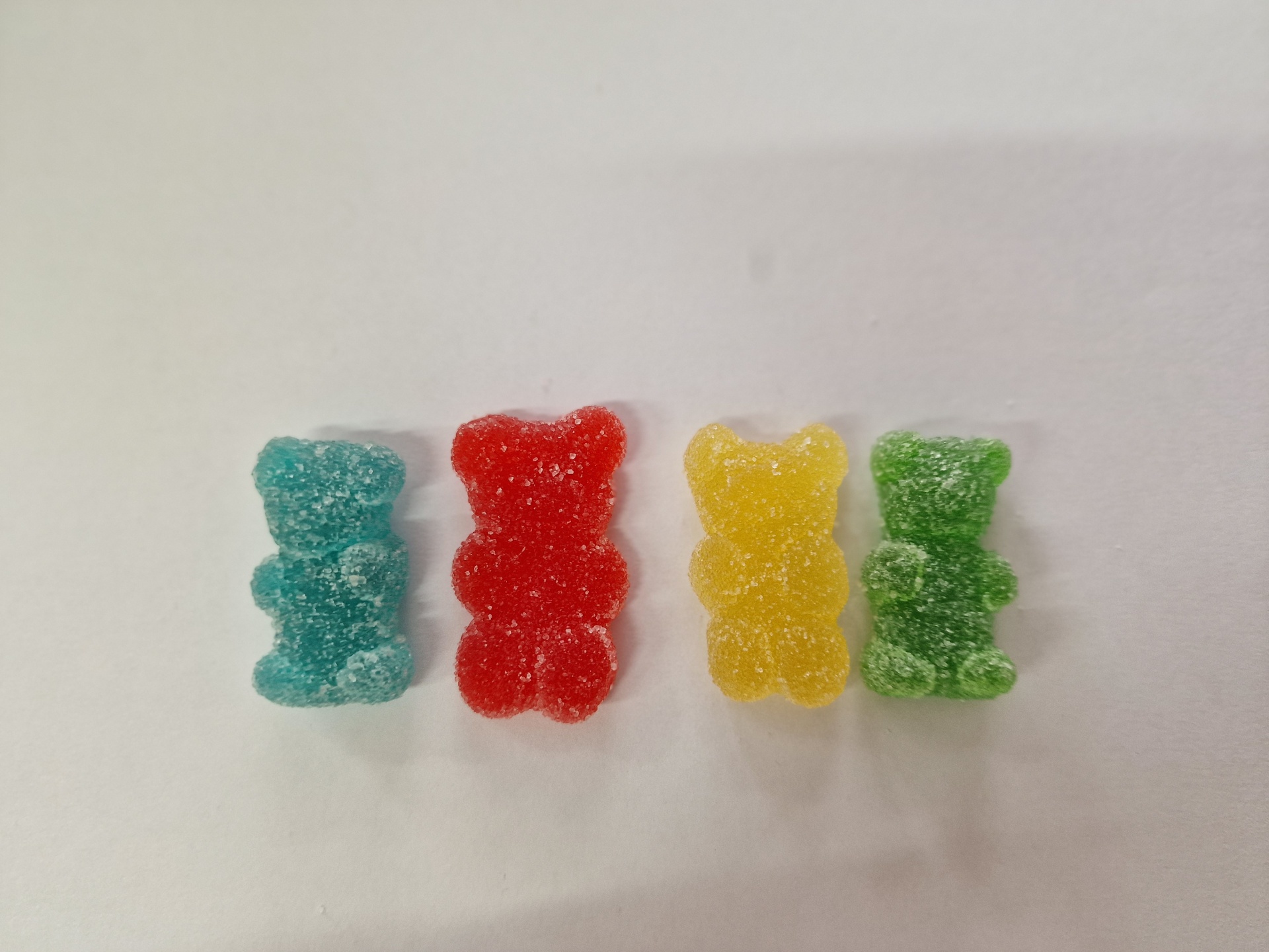 Quatro gomas em forma de ursos coloridos cobertas de açúcar sobre fundo branco