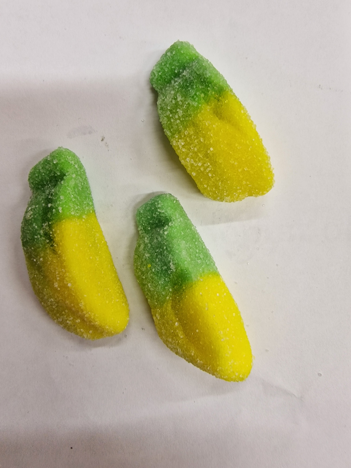 Três gomas verdes e amarelas em forma de dedo cobertas de açúcar