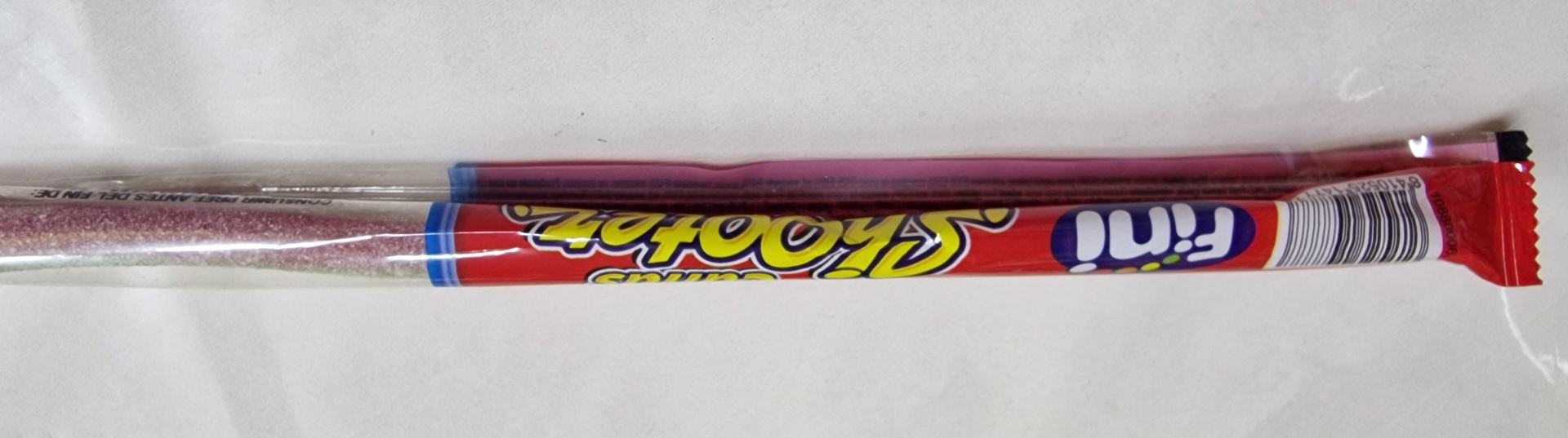 Doce comprido em embalagem plástica vermelha, azul e amarela com texto visível.