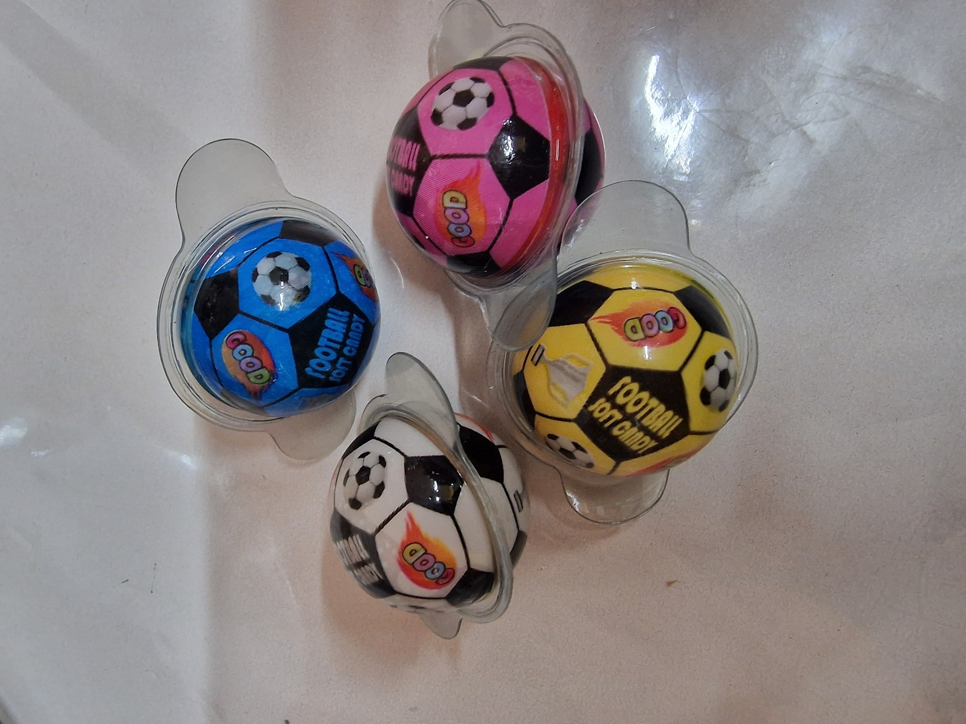 Quatro bolas pequenas de futebol em embalagens plásticas com cores rosa, amarelo, azul e branco