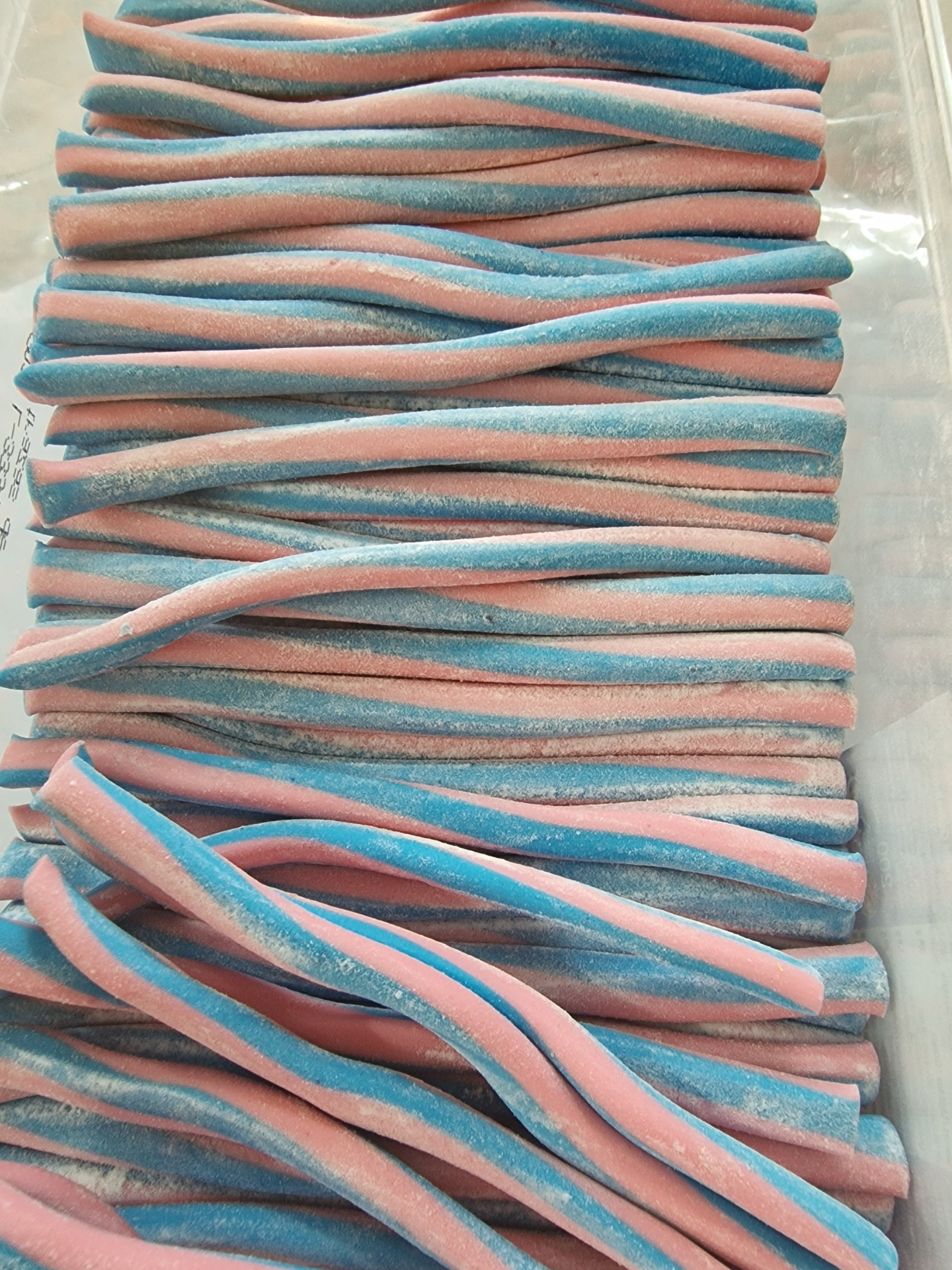 Tiras doces retorcidas rosa e azul claro com açúcar numa caixa de plástico