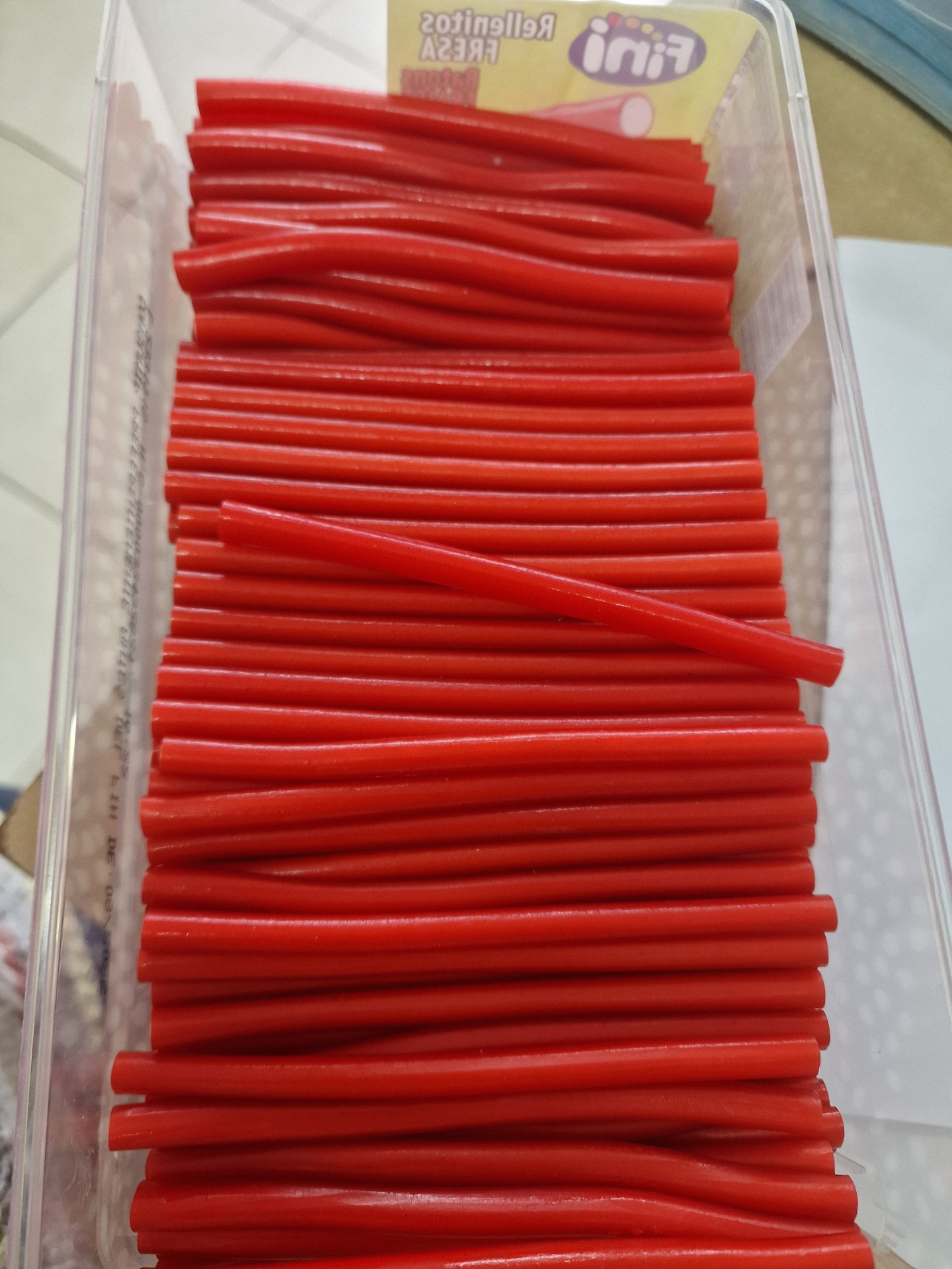 Bastões vermelhos finos em recipiente transparente com rótulo Fini Rellenitos Fresa