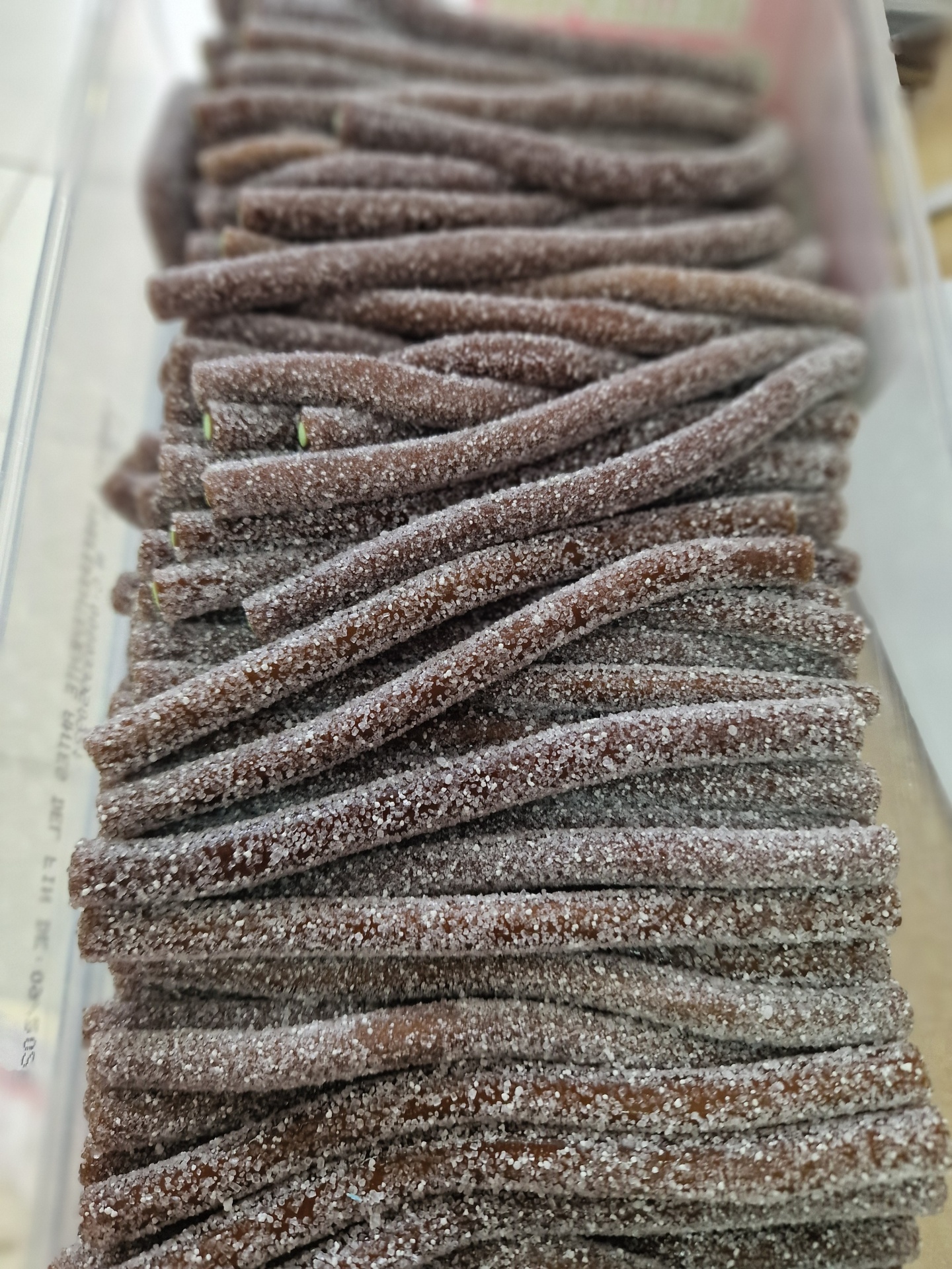 Tiras de doce castanho escuro cobertas de açúcar em recipiente transparente