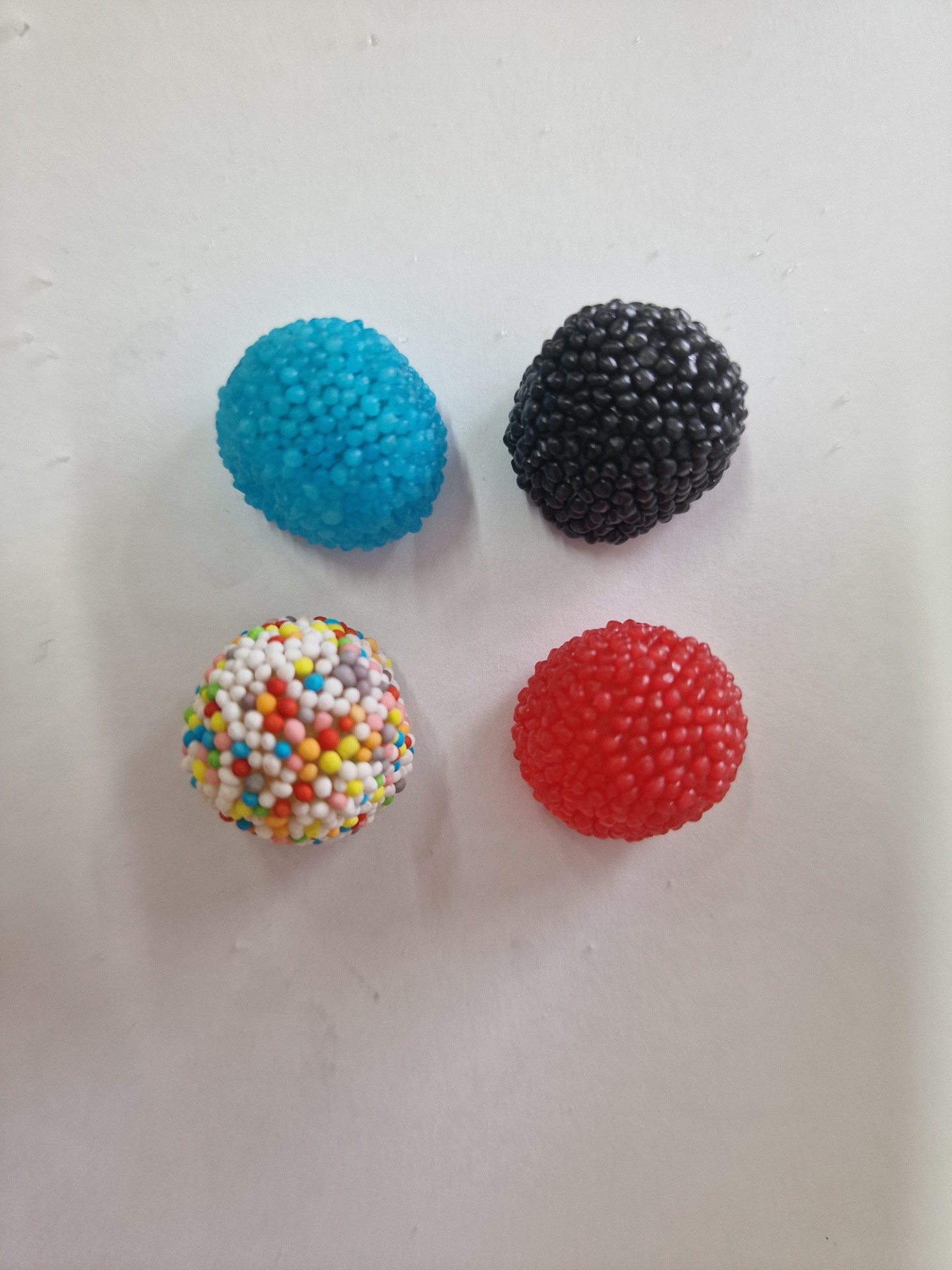 Quatro doces coloridos com textura de esferas, em azul, preto, vermelho e branco multicolorido